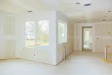 Vista interior de una casa en construcción, con drywall en paredes y techo, grandes ventanales y vista al exterior.