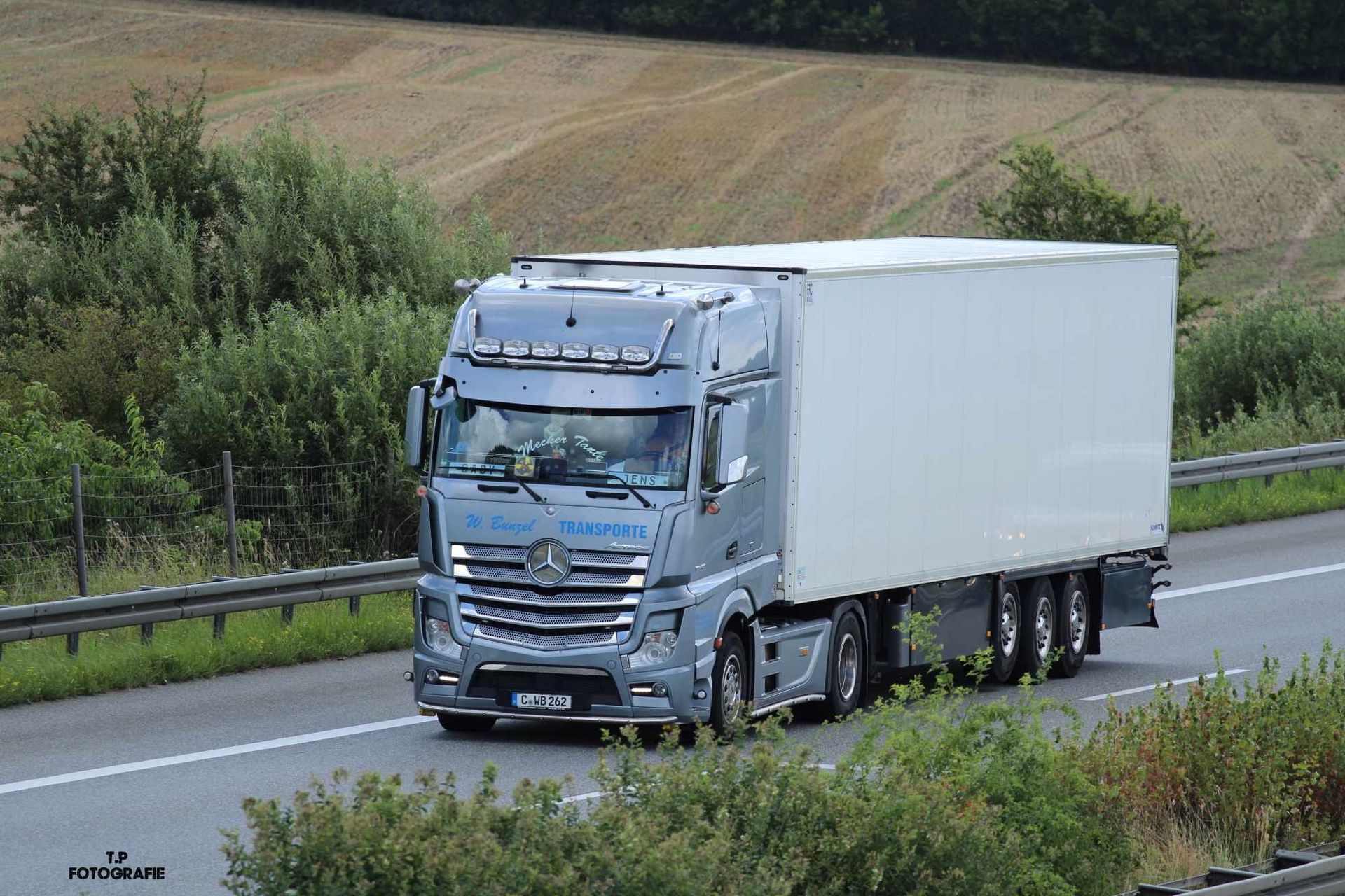 Weißer Sattelzug mit Anhänger auf der Autobahn, Bäume im Hintergrund.
