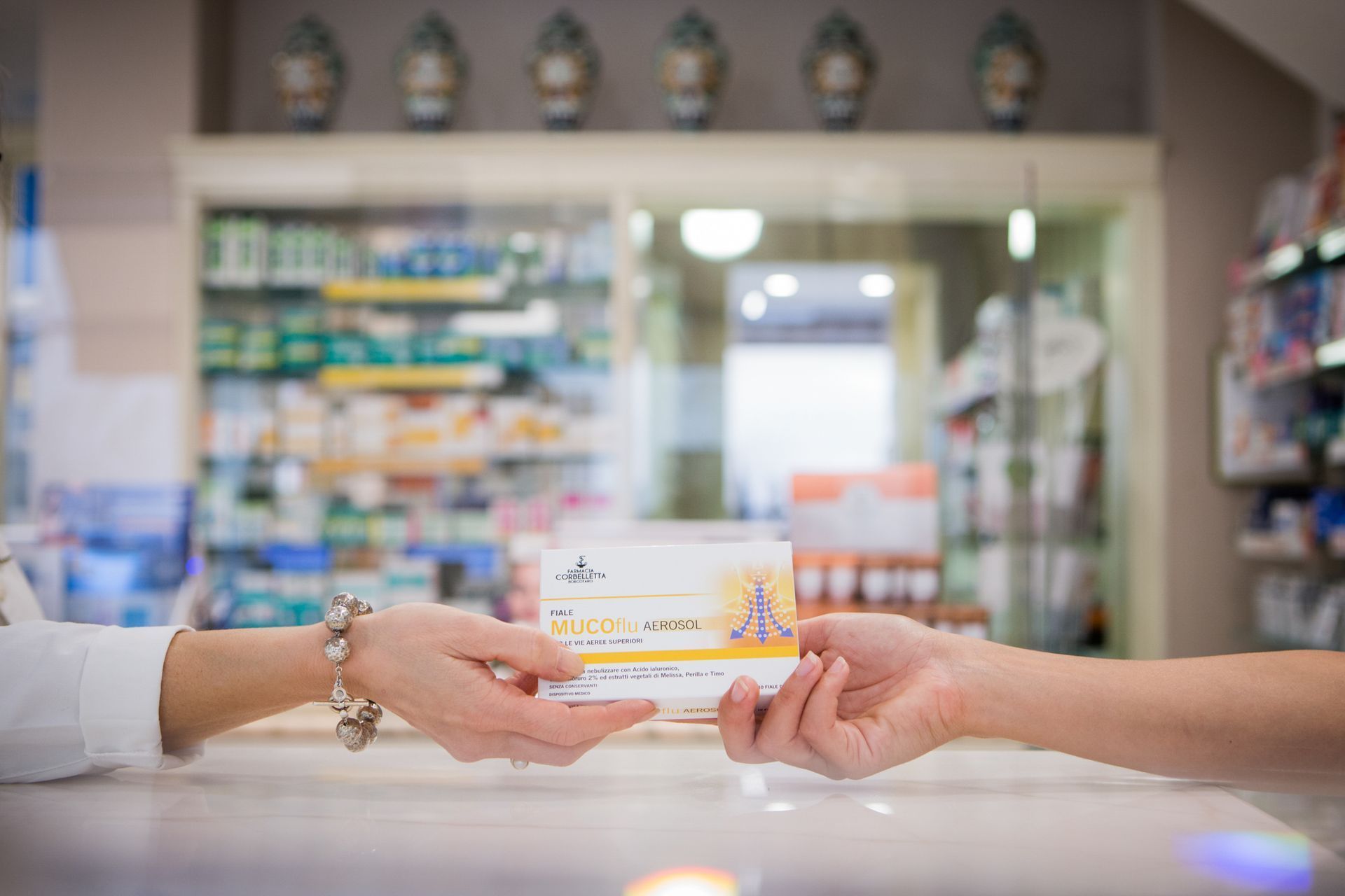 Un farmacista porge una scatola di medicinali a un cliente al di là del bancone della farmacia.