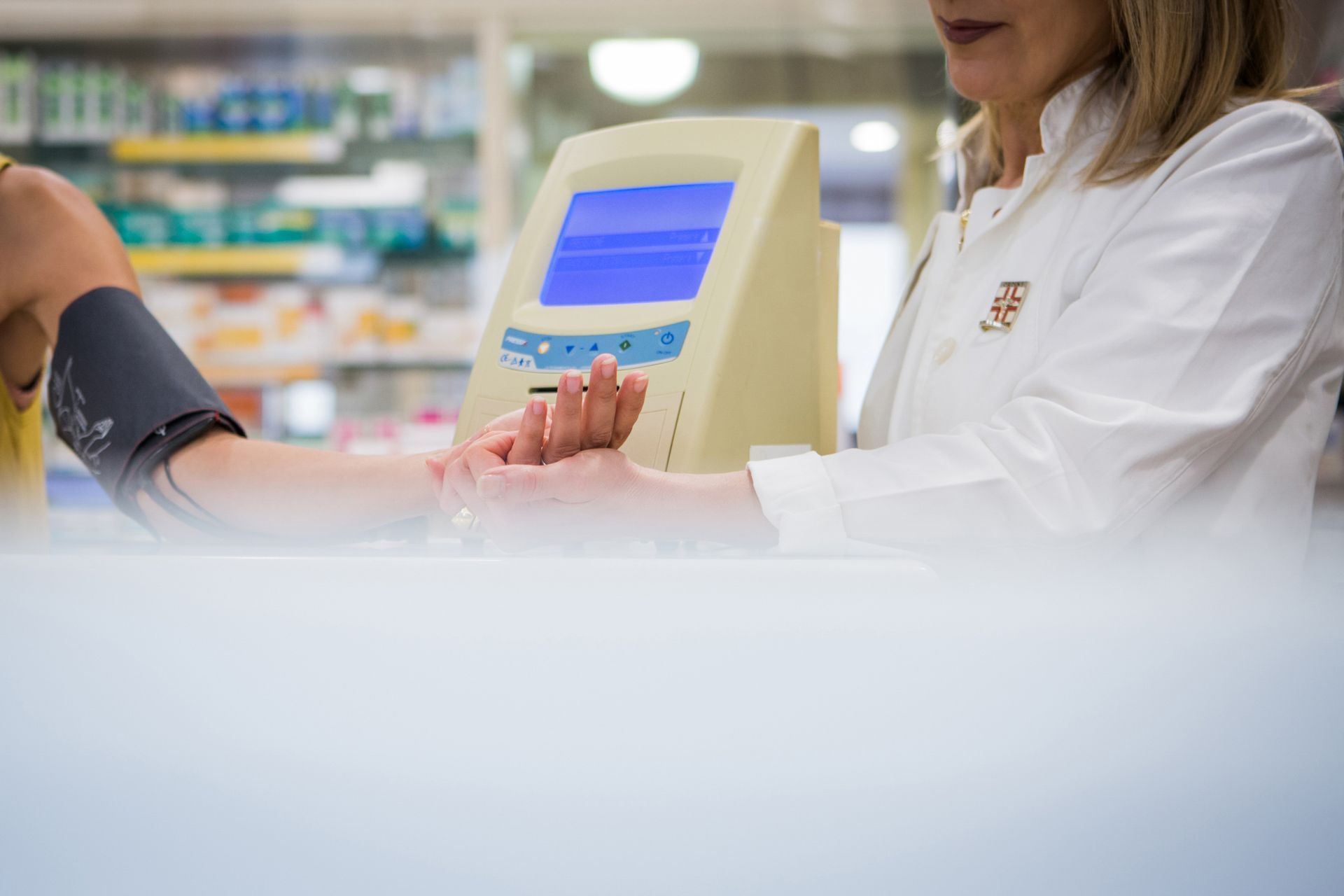 Un farmacista controlla il polso di un paziente mentre un misuratore automatico di pressione sanguigna si trova sul bancone di una farmacia.