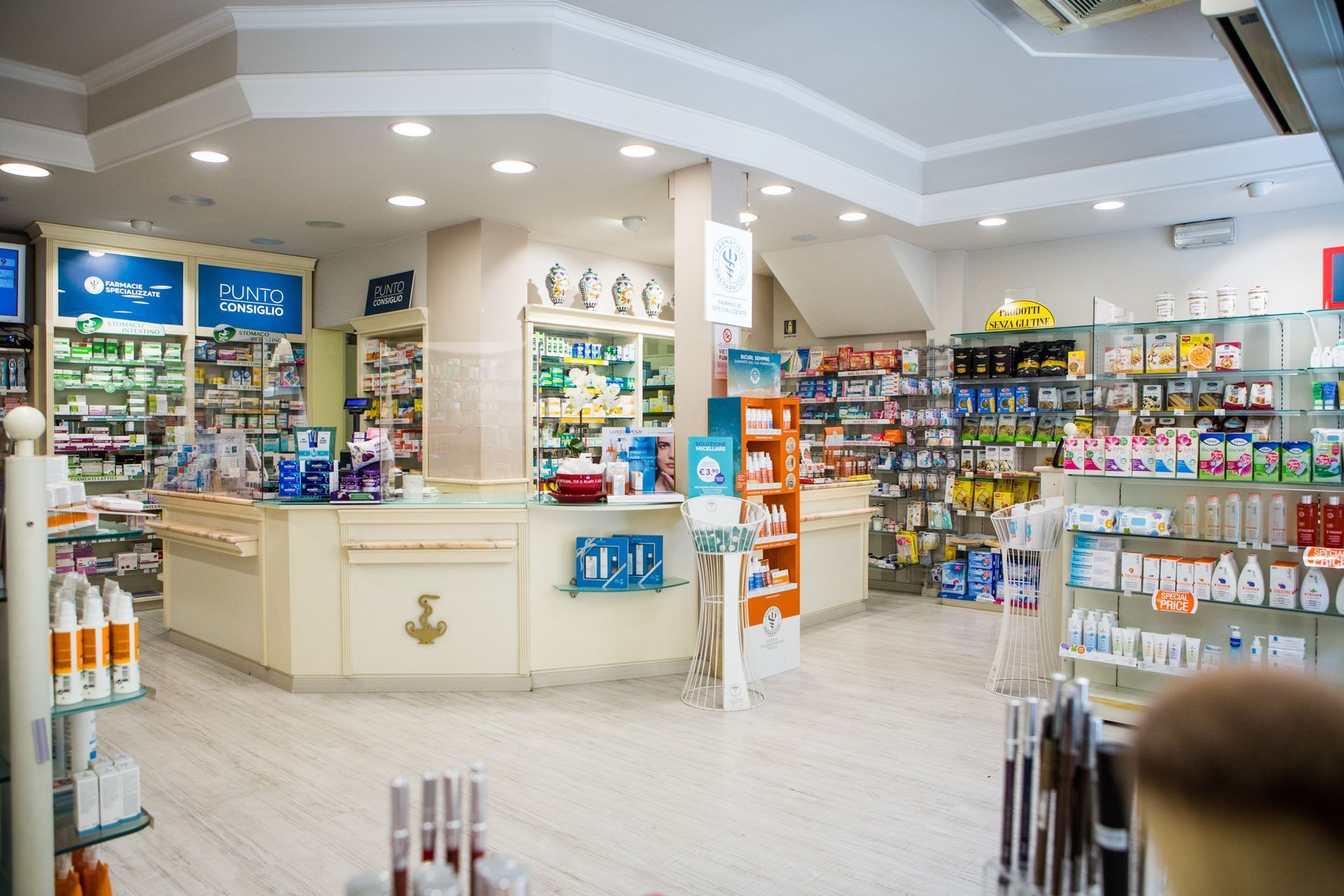 Vista interna della farmacia Corbelletta, luminosa e pulita, con scaffali pieni di prodotti e un bancone al centro.
