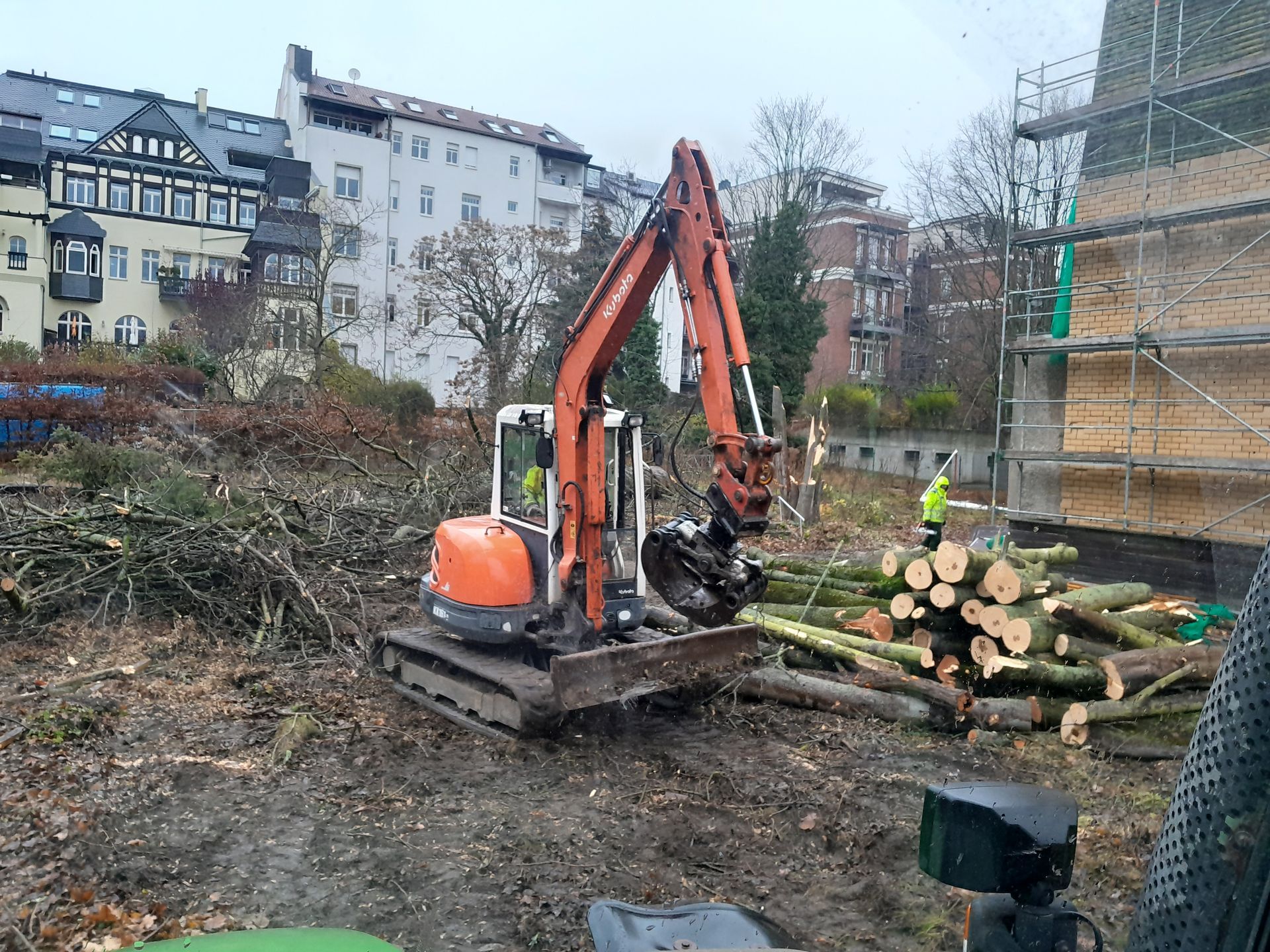 Ein großer orangefarbener Bagger bewegt auf einer Baustelle einen Stapel Baumstämme.