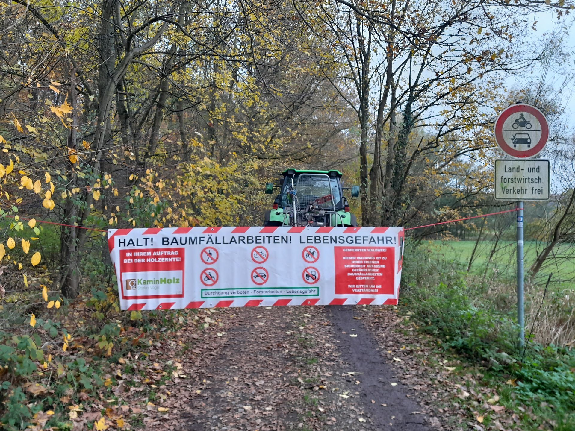 Ein Traktor fährt auf einer unbefestigten Straße neben einem Schild mit der Aufschrift „Halt“ her.