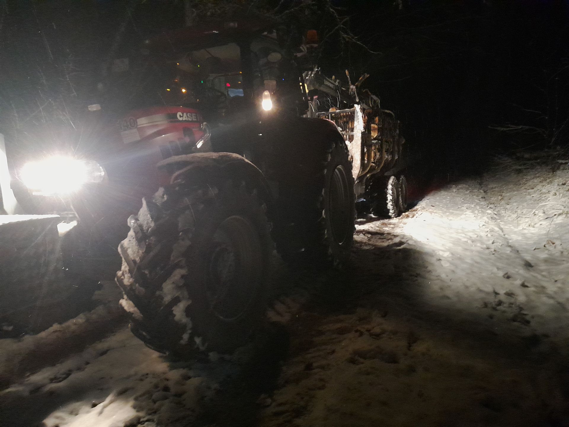 Ein Traktor fährt nachts eine verschneite Straße entlang.
