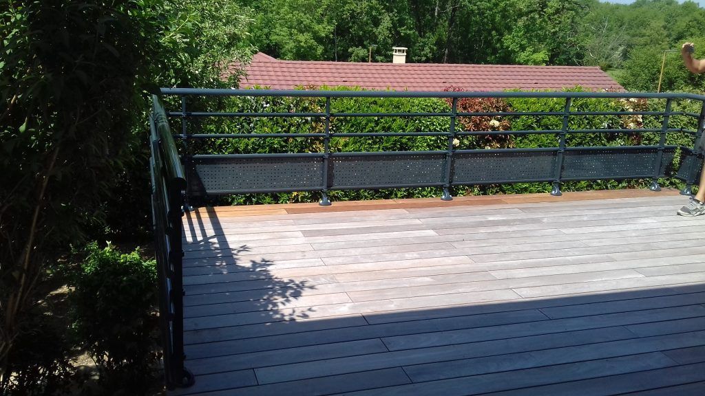 Terrasse en bois ensoleillée avec rambarde noire.
