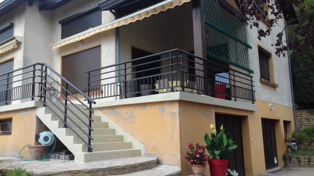 Extérieur d'une maison à deux étages avec escaliers, balcons et plantes en pot.