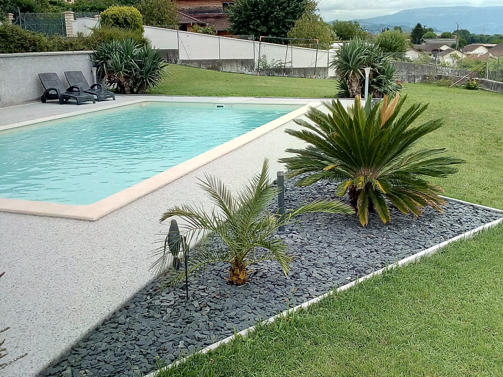 Piscine bordée d'une terrasse en résine agrémentée de plantes.