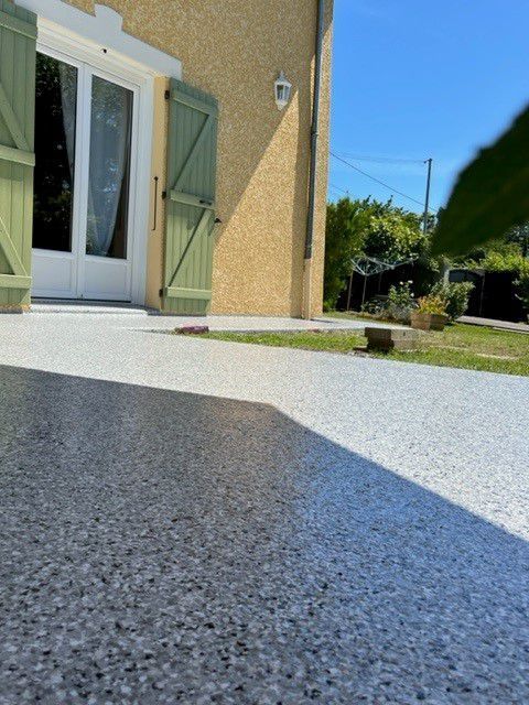Terrasse en résine grise et blanche jouxtant une maison beige.