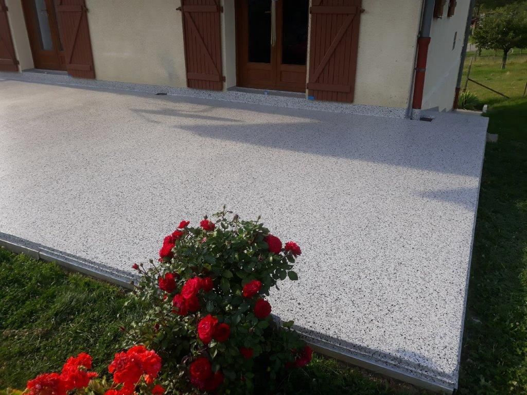 Terrasse en résine et fleurs rouges au premier plan.