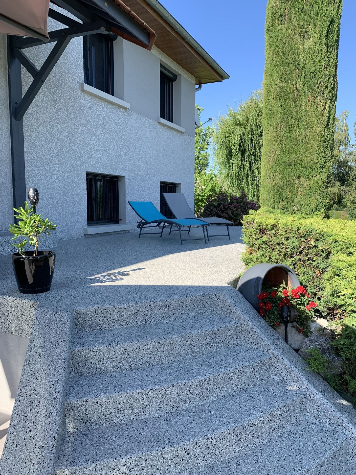 Des marches en résine mènent à un patio ensoleillé jouxtant une maison blanche.