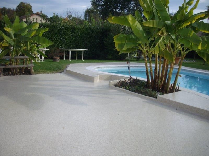 Bord de piscine aménagé avec un sol en résine et de la végétation.