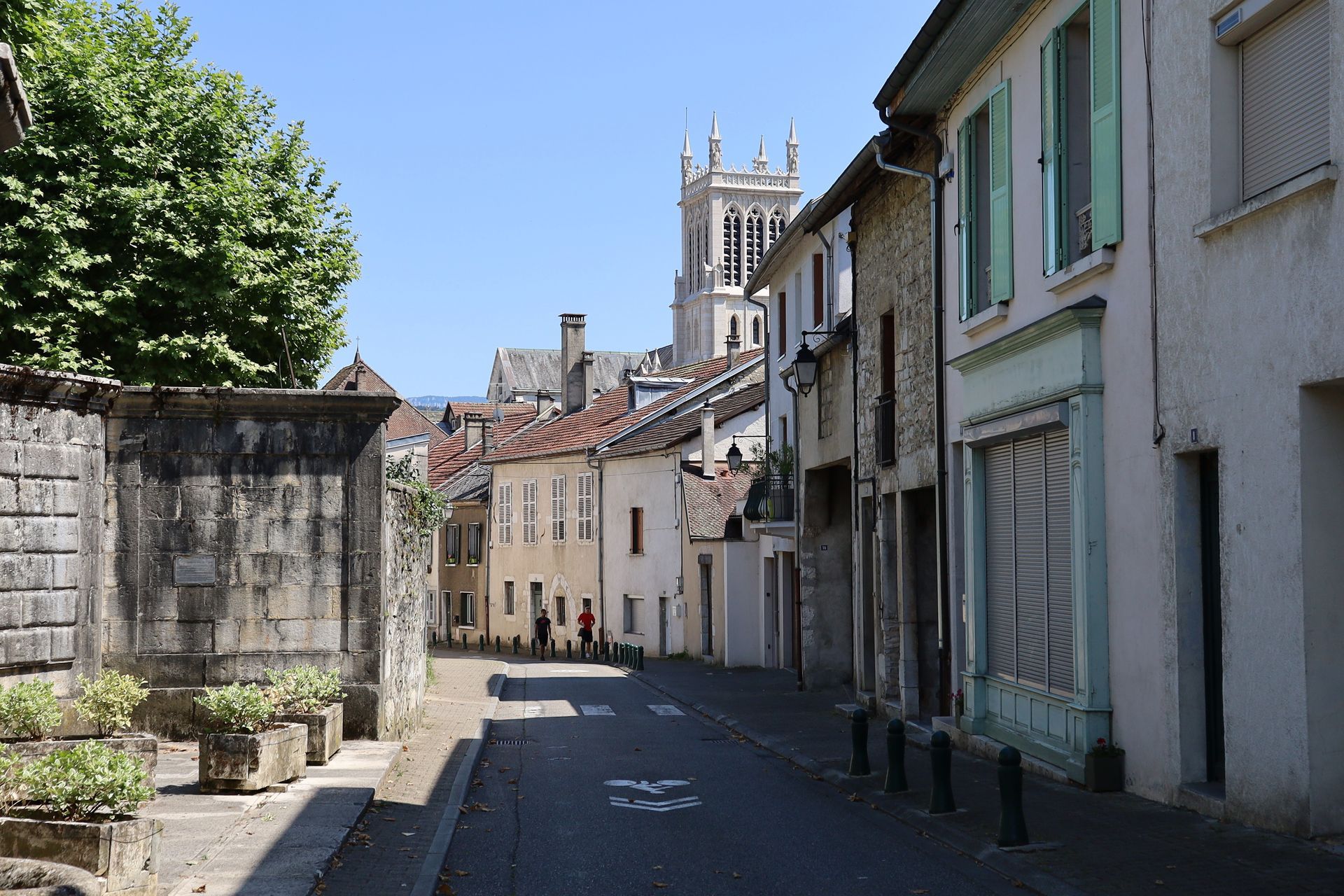 Rue pavée étroite bordée de vieux bâtiments en pierre et d'un clocher sous un ciel bleu limpide