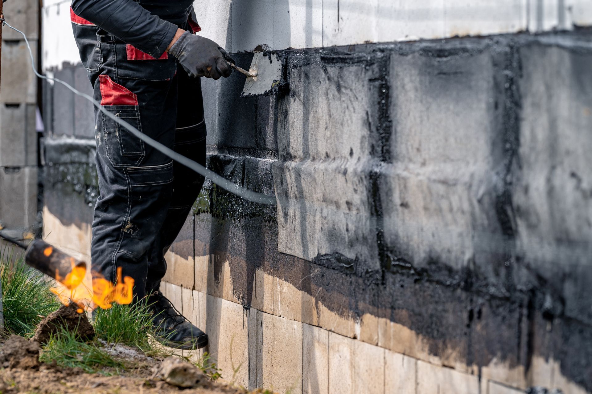 Un ouvrier applique un enduit noir sur un mur en brique à l'extérieur.