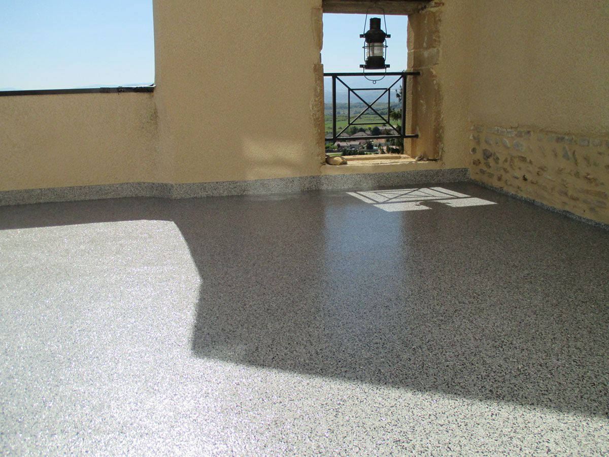 Une terrasse en résine entourée par des murets en pierre et un garde-corps en métal.