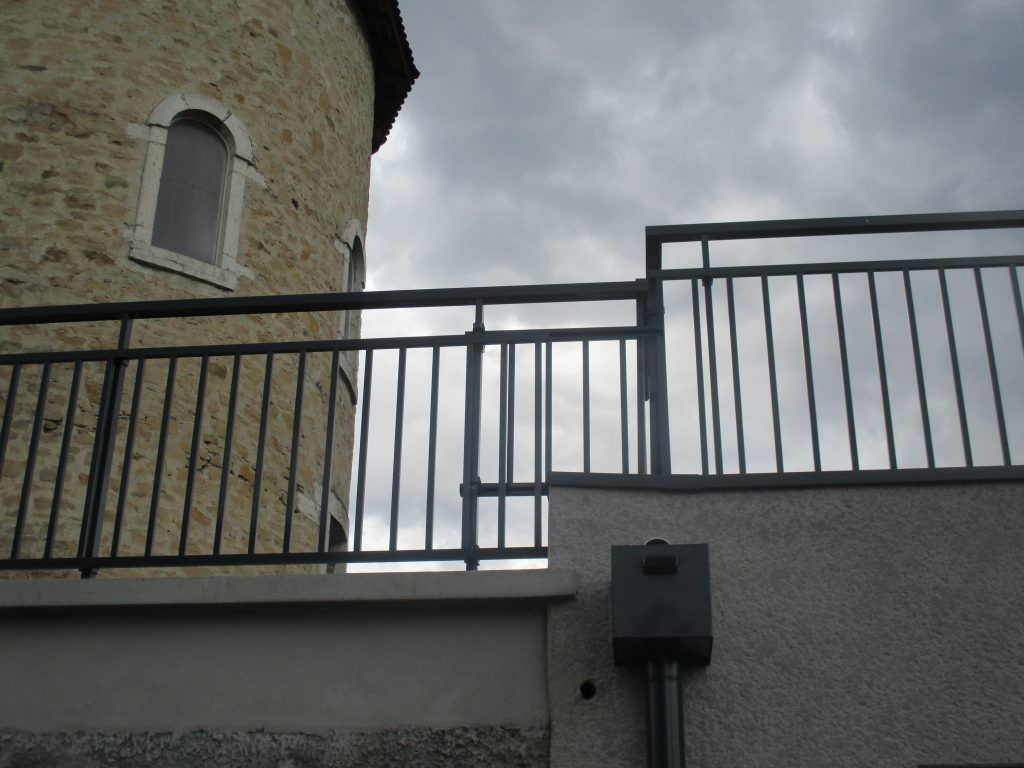 Tour de pierre derrière une balustrade noire se détachant sur un ciel nuageux