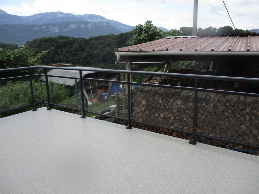 Terrasse sur le toit avec balustrade noire donnant sur des collines verdoyantes et un paysage montagneux nuageux.