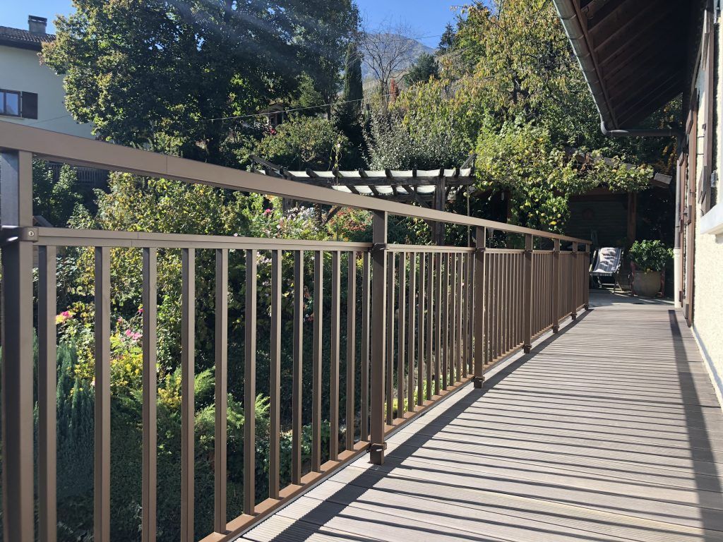Allée avec rambardes métalliques et jeux d'ombre et de lumière du soleil à travers une végétation luxuriante.