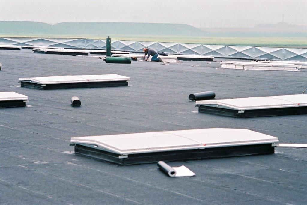 Toit-terrasse percé de plusieurs puits de lumière et aérations blancs sous un ciel nuageux.