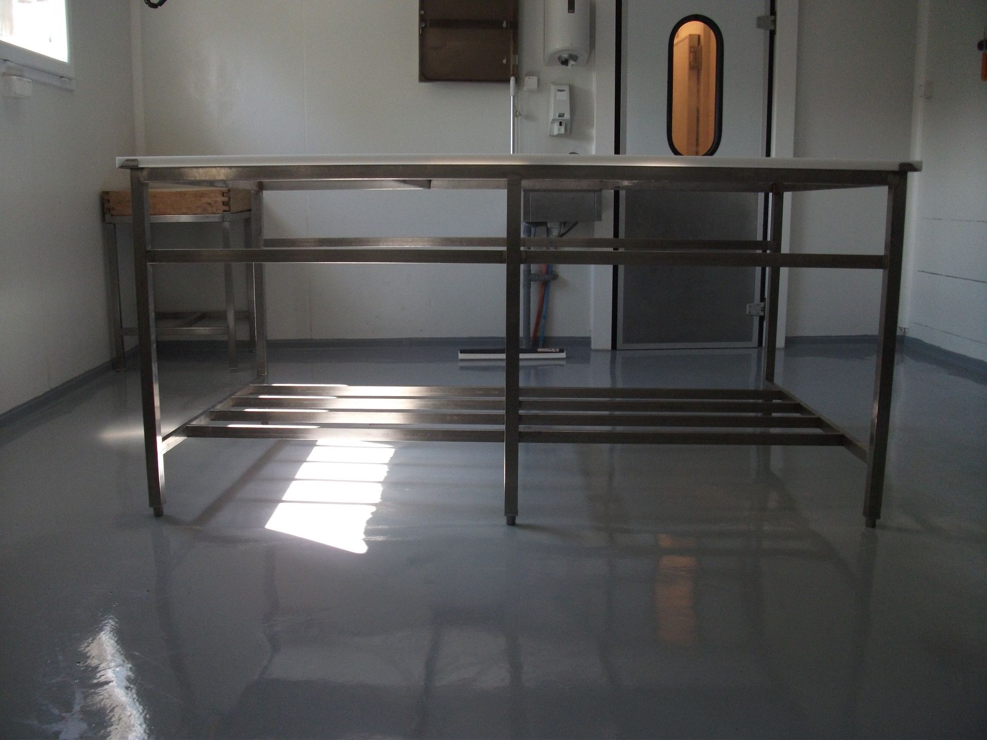 Table métallique vide dans une cuisine industrielle lumineuse, le soleil se reflétant sur le sol