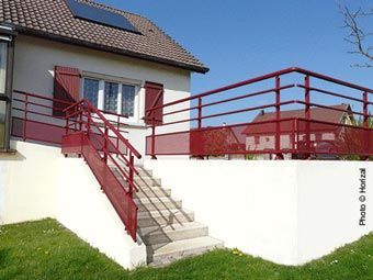 Un escalier extérieur à rampe rouge mène à une maison blanche avec une balustrade rouge.