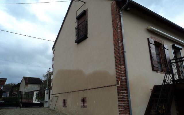 Façade d'une maison couleur crème avec une tache d'humidité sur le bas.