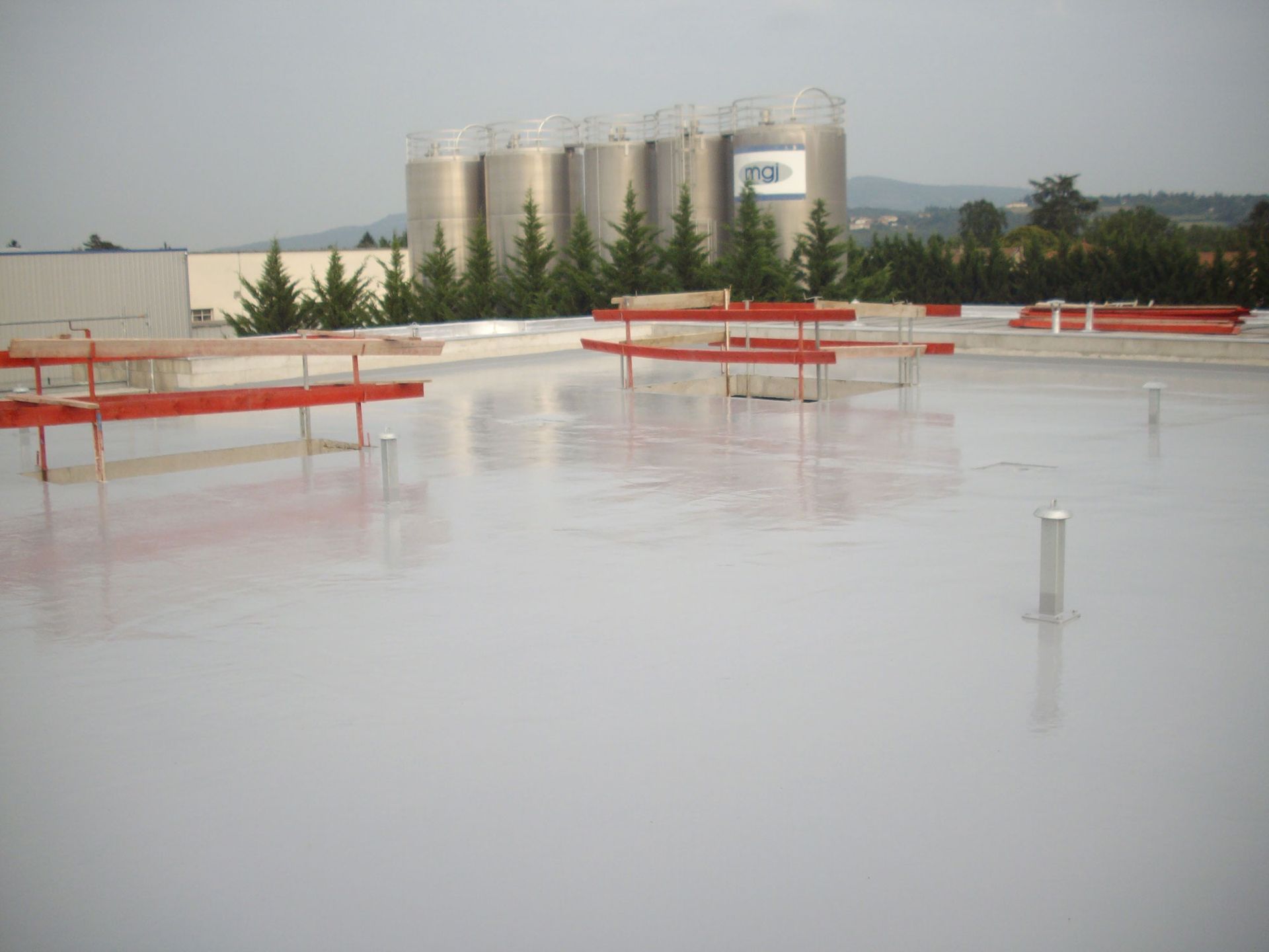 Toit industriel avec revêtement blanc en résine et des barrières rouges posées autour de trous.