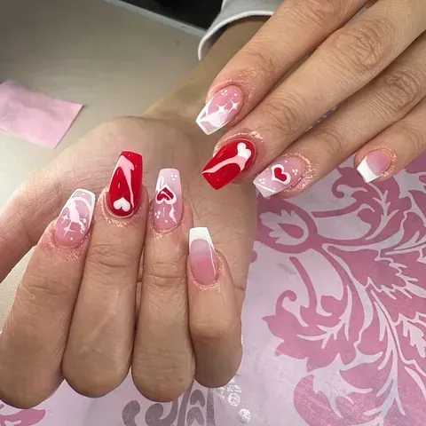Las uñas de una mujer están pintadas de rojo y rosa con un diseño de llave y corazón.