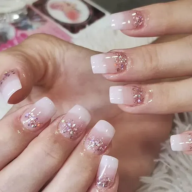 Un primer plano de las uñas de una mujer con brillo y diamantes de imitación.