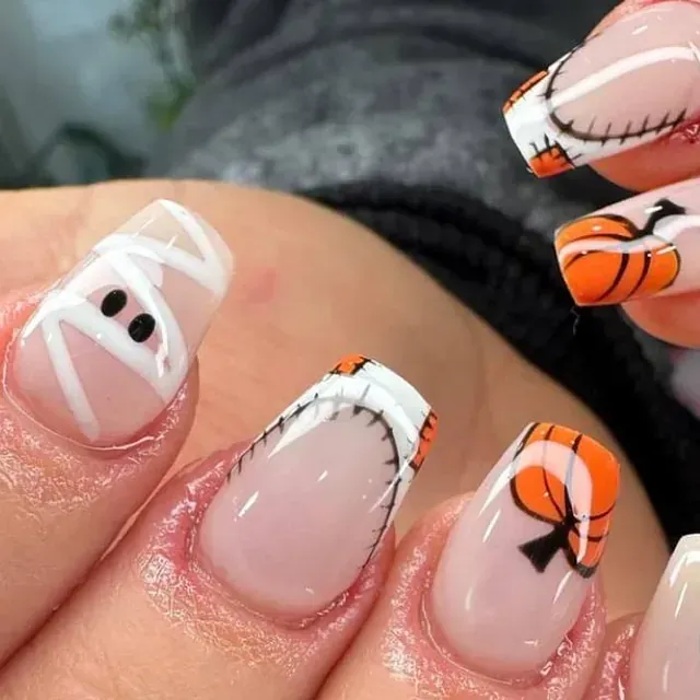 Un primer plano de las uñas de una persona con un diseño de momia y calabaza.