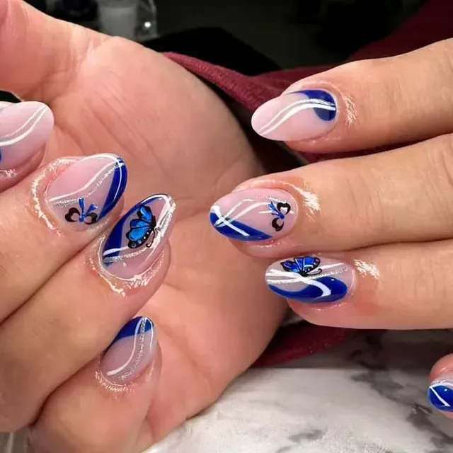 Un primer plano de las uñas de una mujer con un diseño de mariposa azul.