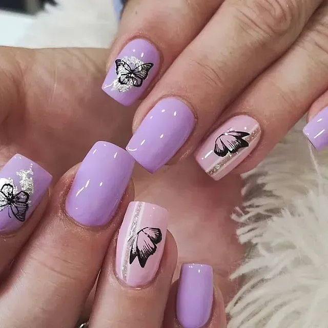 Las uñas de una mujer son de color morado y rosa con mariposas en ellas.