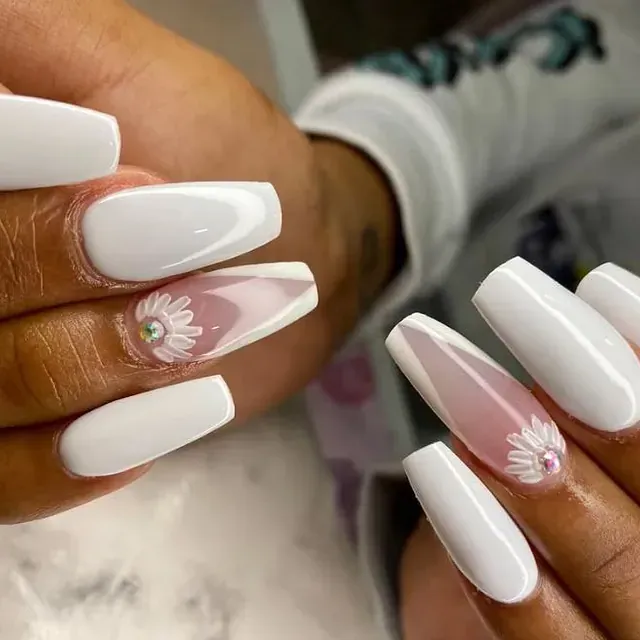 Un primer plano de las uñas de una persona con uñas blancas y un diseño floral.