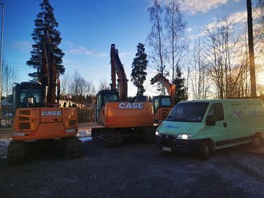 Kaksi oranssia CASE-kaivinkonetta valkoisen pakettiauton vieressä sorakentällä auringonlaskun aikaan