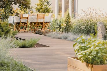 Ensemble de salle à manger en bois pour terrasse, bordant une allée de jardin sinueuse ornée de verdure luxuriante et de plantes en pot.