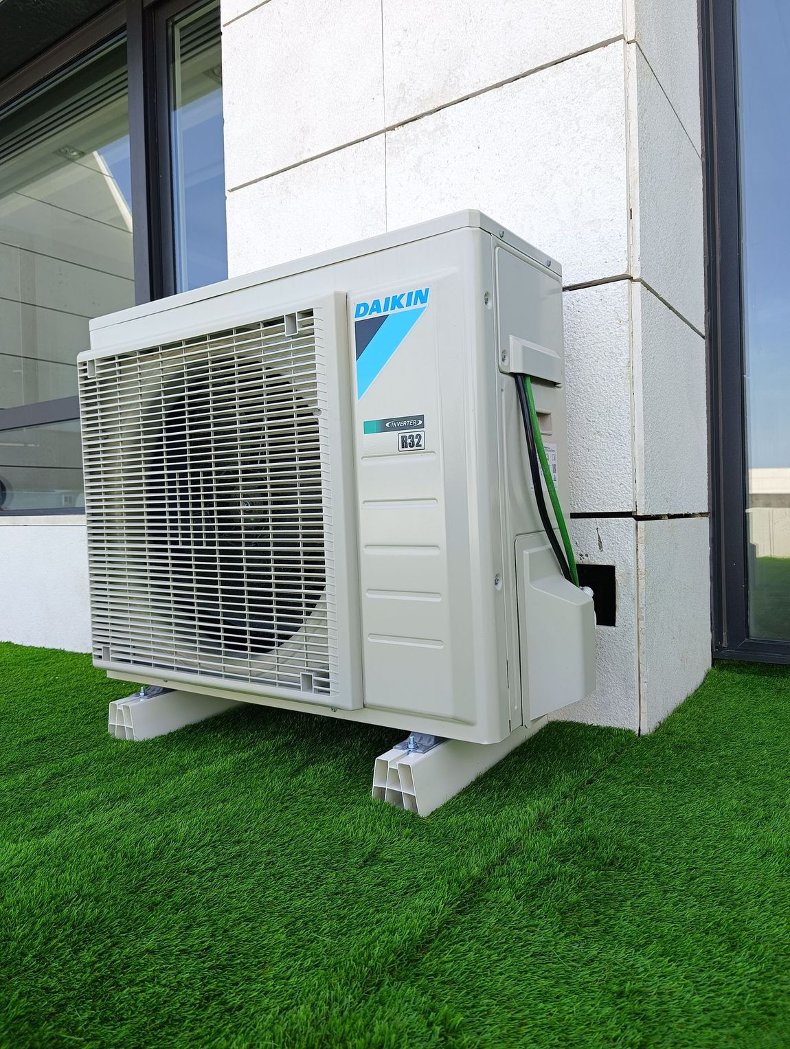 Un acondicionador de aire Daikin está ubicado sobre un exuberante césped verde al lado de un edificio.
