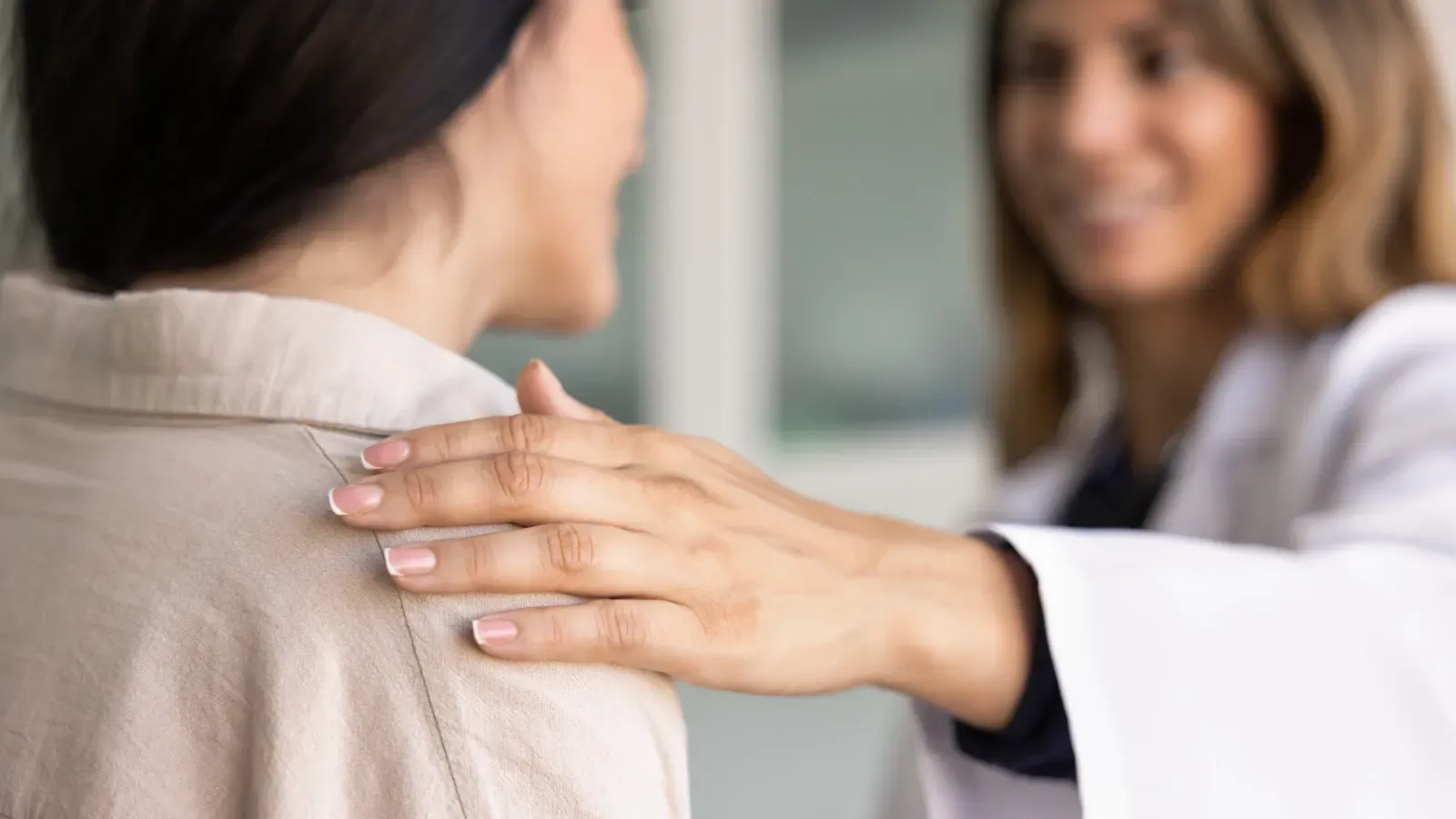 Ein Arzt beruhigt eine Patientin, indem er ihr in einer Klinik die Hand auf die Schulter legt.