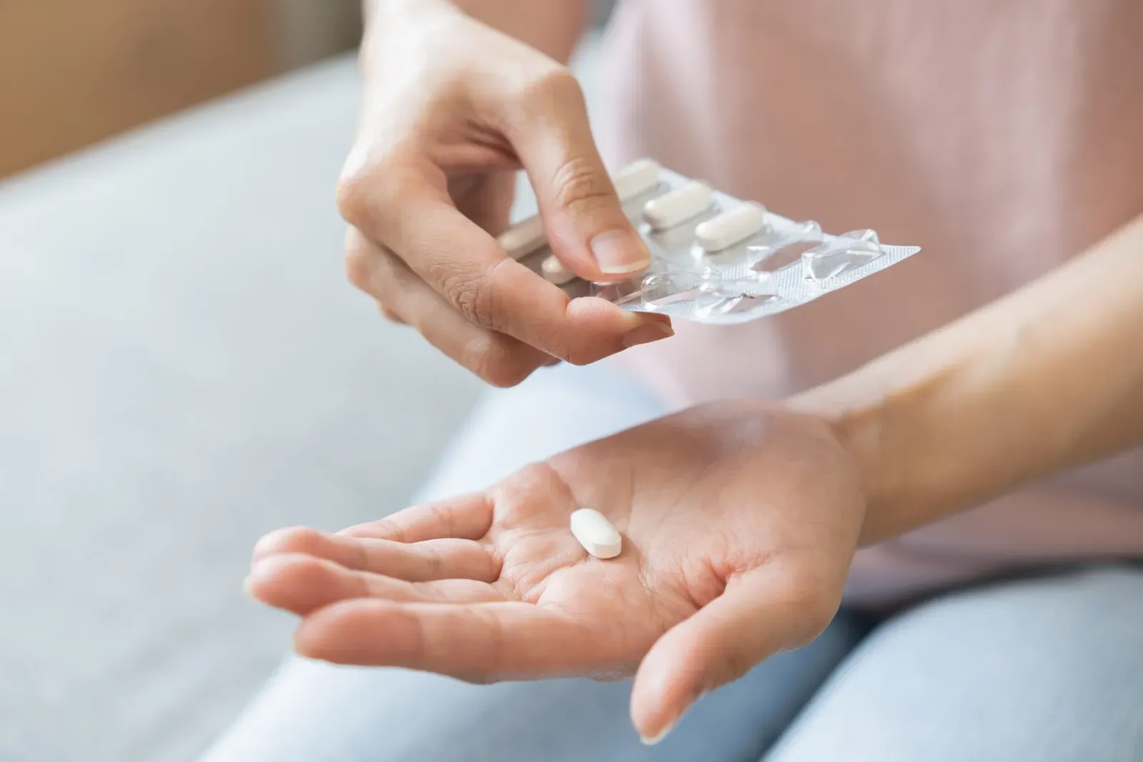 Eine Person legt eine weiße Pille aus einer Blisterpackung in ihre offene Handfläche