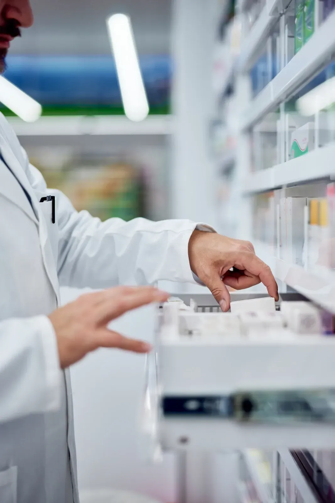 Ein Apotheker greift in eine Apothekenschublade neben Regalen mit Medikamentenflaschen.