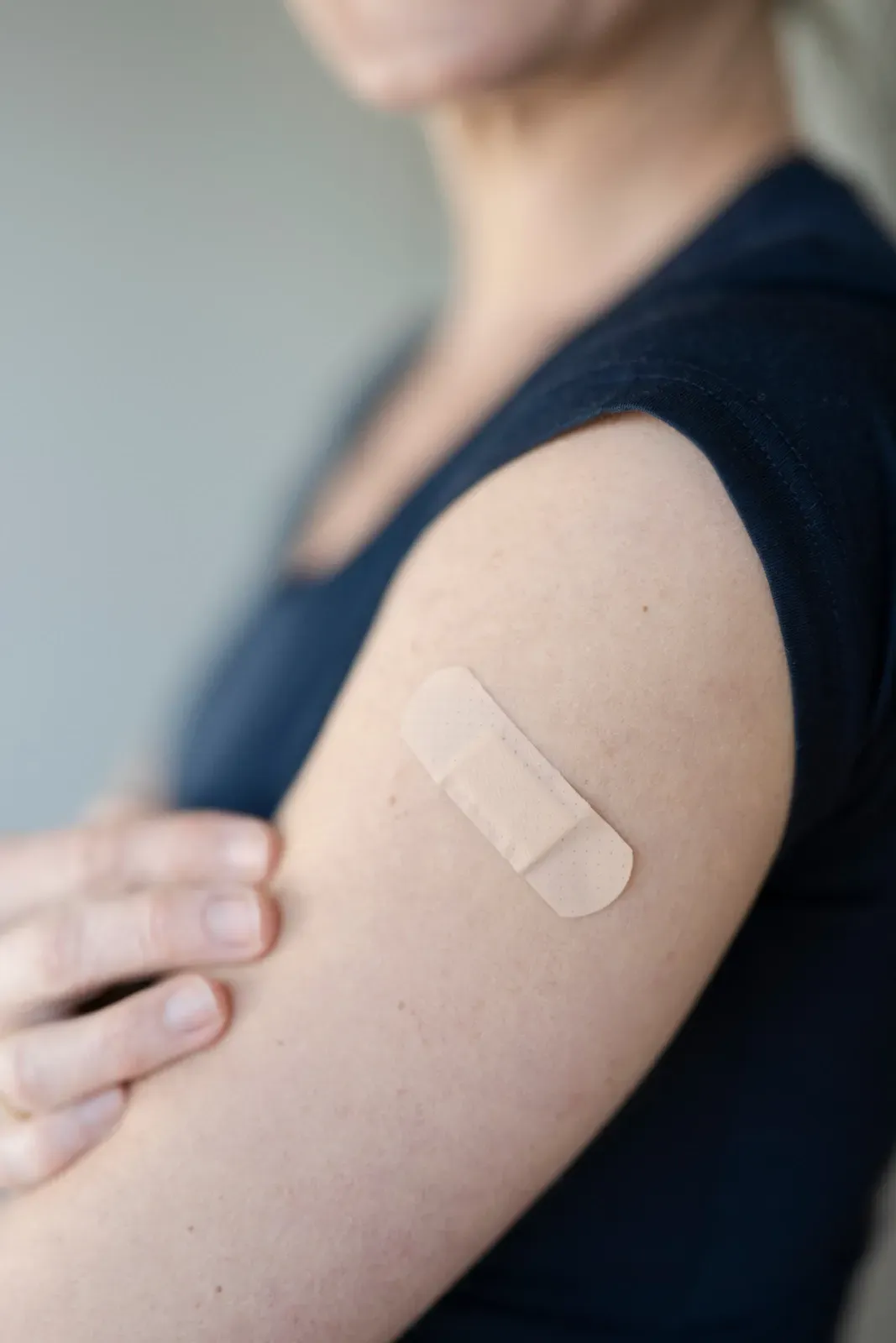 Arm mit beigefarbenem Verband am Oberarm, Hand berührt die Schulter in einem dunklen Hemd.