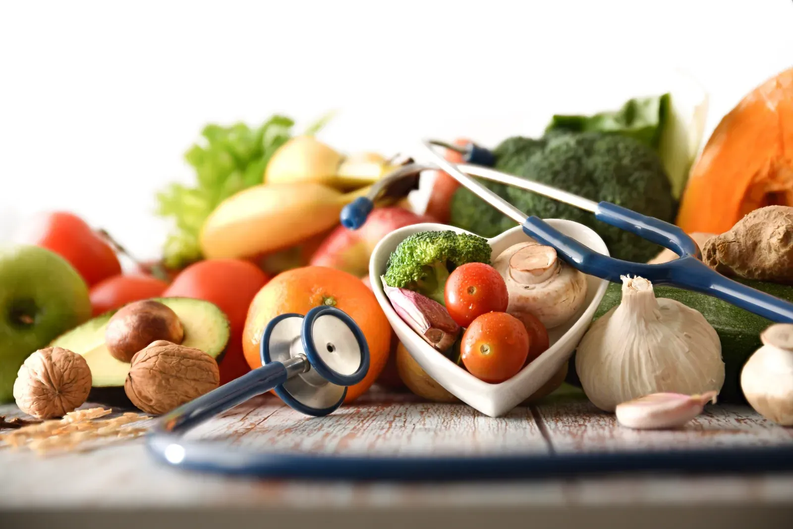 Frisches Gemüse, Knoblauch und ein Stethoskop arrangiert auf einem Tisch, suggerieren gesunde Ernährung und medizinische Versorgung.