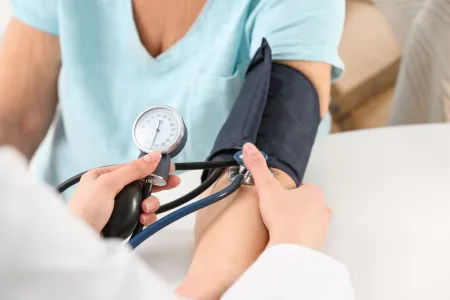 Eine medizinische Fachkraft misst den Blutdruck eines sitzenden Patienten mit einer Blutdruckmanschette und einem Manometer am Arm.