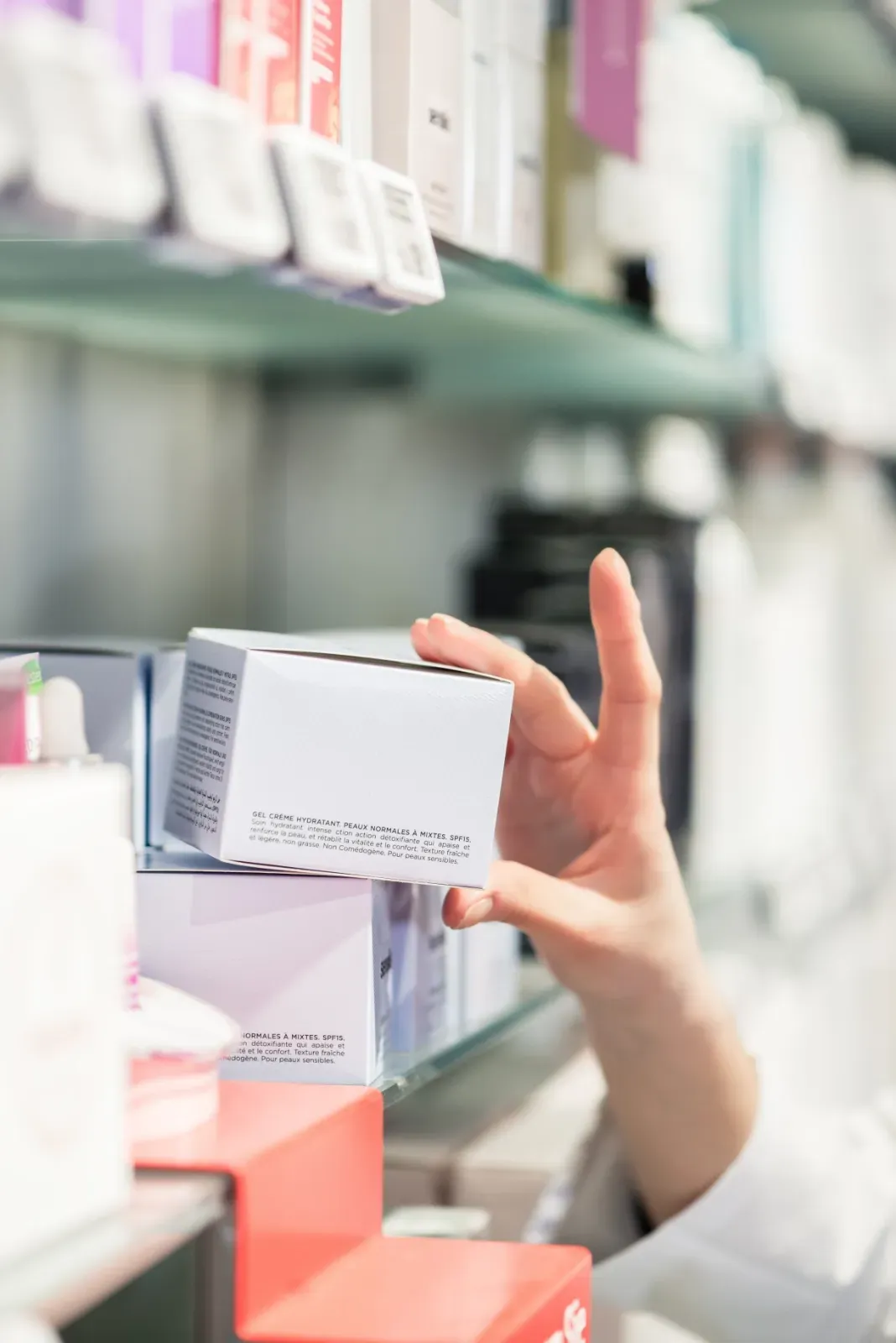 Eine Hand greift nach einer weißen Produktverpackung in einem Apothekenregal.