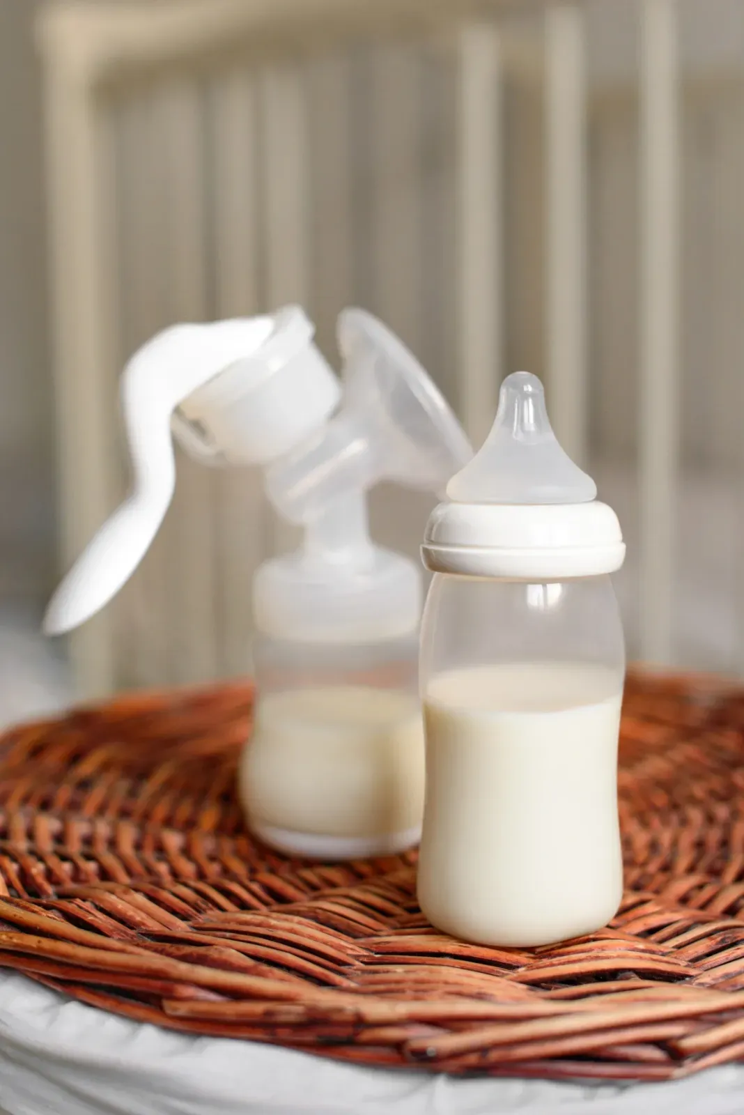 Zwei Babyflaschen auf einer Weidenmatte, eine mit Sprühverschluss und die andere mit Saugerverschluss, gefüllt mit Milch.