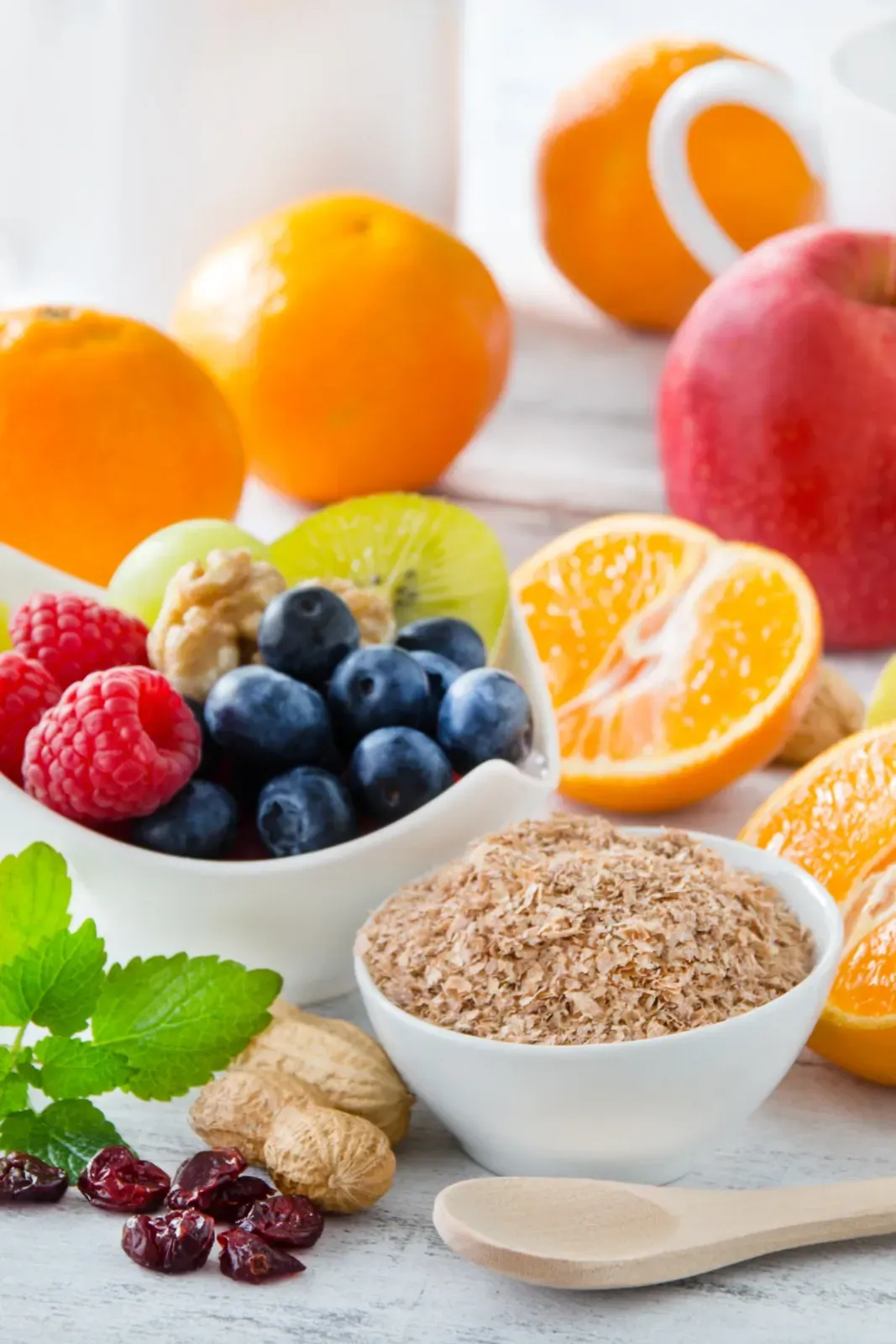Verschiedene frische Früchte und Haferflocken in Schüsseln mit Beeren, Zitrusfrüchten und einem Holzlöffel auf einer weißen Oberfläche