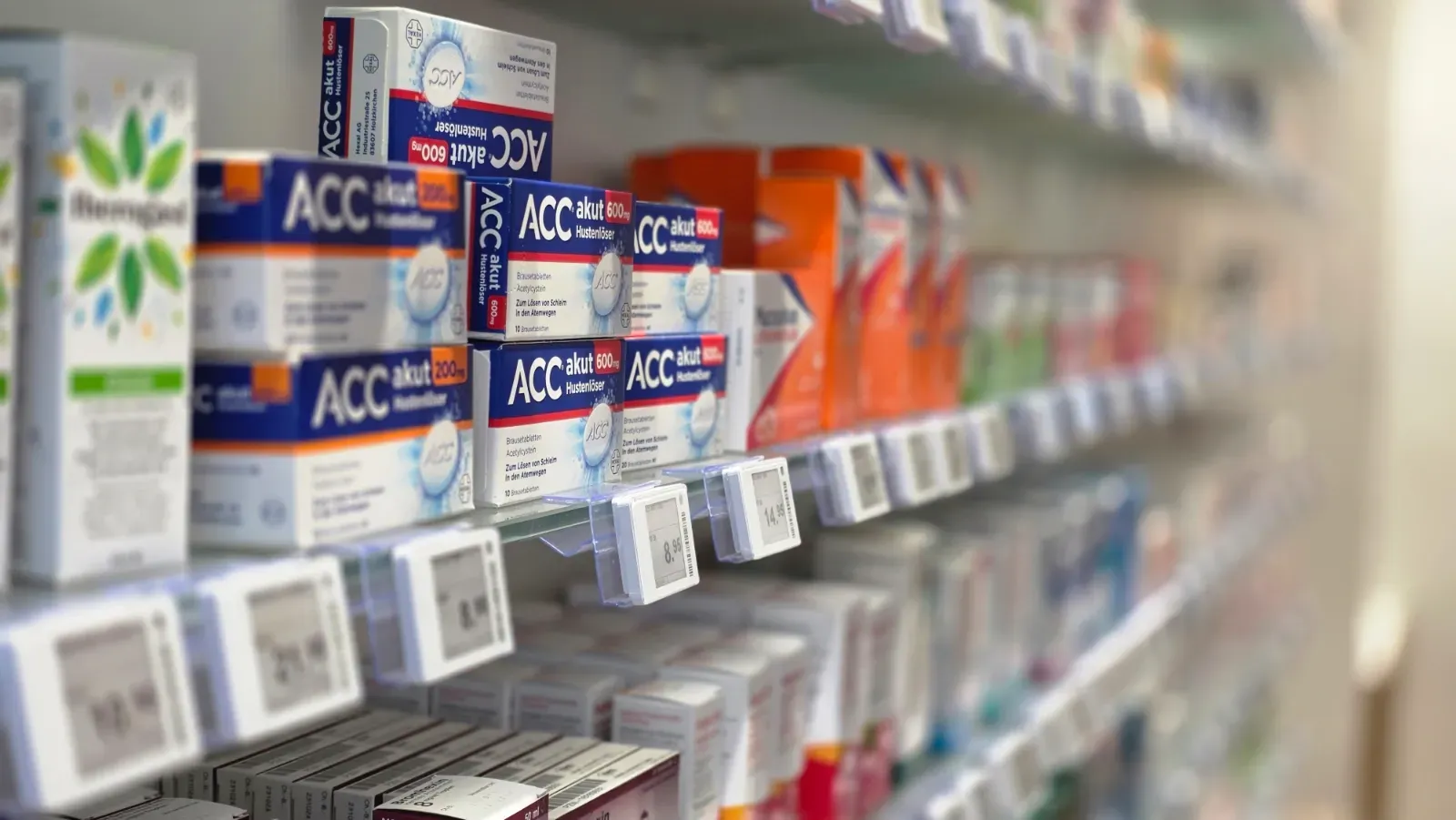 Reihe bunter Medikamentenschachteln in Apothekenregalen mit Preisschildern im unscharfen Fokus