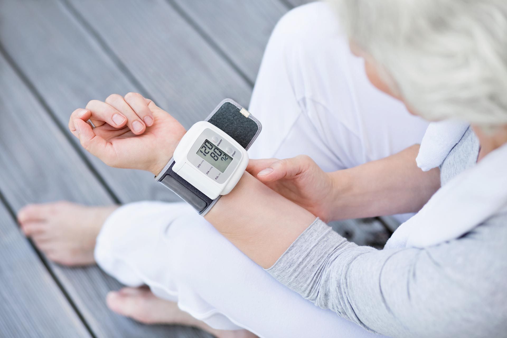 Eine Person schaut auf ihre Armbanduhr mit Digitalanzeige, während sie auf einem grauen Boden sitzt.