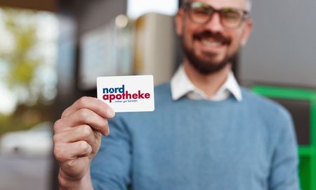 Ein lächelnder Mann im blauen Pullover hält eine Nordecke-Karte in die Kamera.