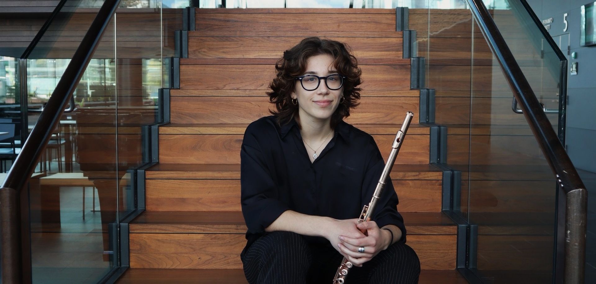 Person spielt eine Silberflöte, Hände auf den Tasten, in einem Innenraum.