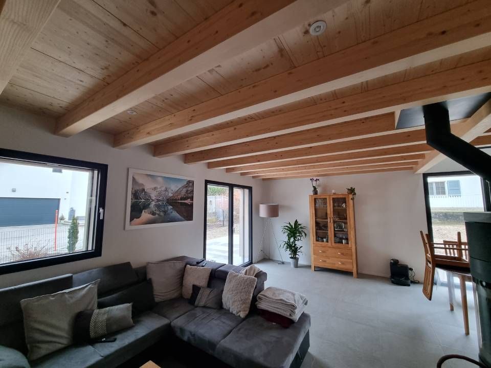 Salon moderne avec poutres apparentes au plafond, canapé d'angle gris, meuble en bois, chaises de salle à manger et cheminée.