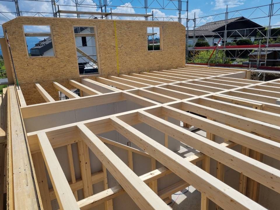 Un chantier de construction montrant des solives de plancher en bois pour une structure de bâtiment avec des panneaux muraux en OSB en arrière-plan.
